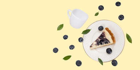 A piece of blueberries cheesecake on a falling white  ceramic plate with falling white ceramic cup and some flesh bleuberries and green leaves on soft yellow background. Food levitation concept.の写真素材