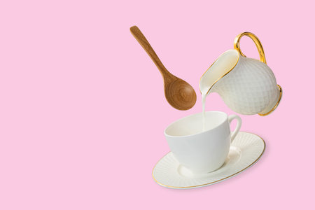 Levitation white coffee cup and saucer with milk pouring from a milk jug with a floating wooden spoon. Isolation on soft pink color background. Levitation food photography concept.の写真素材