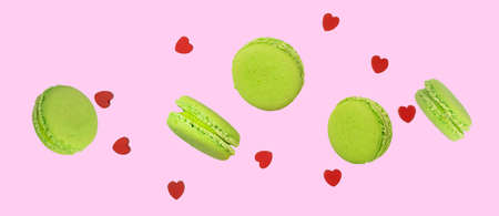 Pieces of green pistachio macaroons or french macarons levitating among small red wooden hearts on a soft pink background. Levitation food photography concept.の写真素材