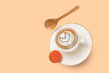 A white porcelain cup with cappuccino coffee and a gold rimmed saucer with a wooden spoon and an orange macaroon levitating on soft orange surface background.の写真素材