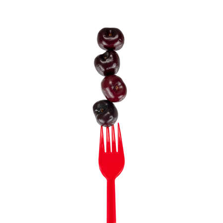 A stack of four fresh cherries balancing on a red fork.の写真素材