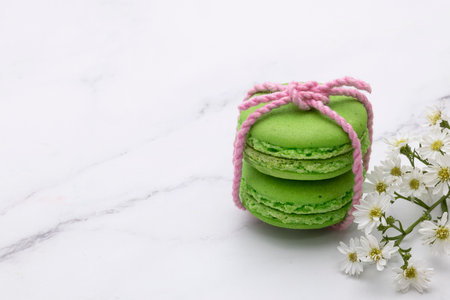 Closed up of two green macaroons tied with soft pink thread with beautiful tiny white flowers. Marble top background.の写真素材