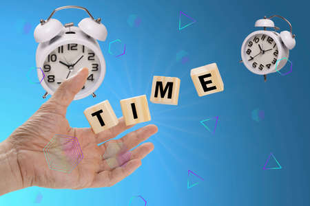 A hand reaching out to catch falling wooden cubes labelling with a text 'time' with moving away white alame clocks. Time concepts.の写真素材