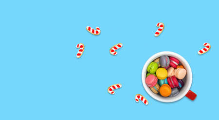 Colorful mini macaroons in a cup with sugar cane biscuits on blue background.