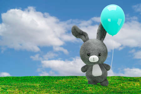 3d render illustration of stuffed toy rabbit with a blue balloon on a grass field.の写真素材