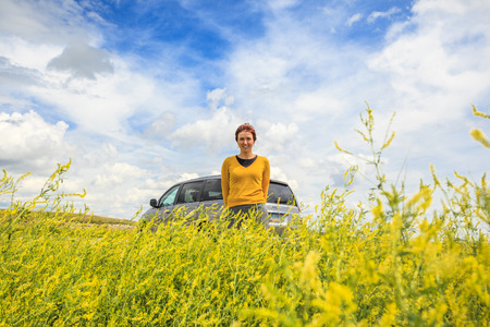 Happy woman with her car among canola fieldの写真素材