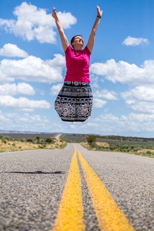 Happy woman jumping over empty american road.