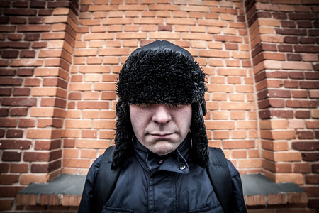 Funny disappointed man hiding in his cap at brick backgroundの写真素材