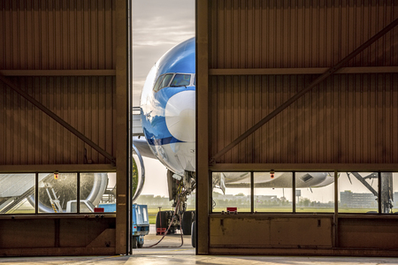 Blue airplane in front of half opened door to hangarの写真素材