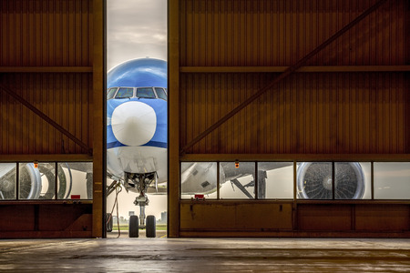 Blue airplane in front of half opened door to hangarの写真素材
