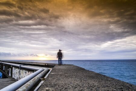 People walking on a pier toward the sunrise