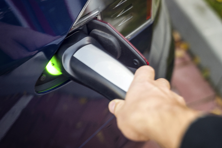 Man's left hand holding modern electric car charger outlet.