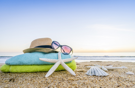Summer accesories as sunglasses, towels, hat, sun block, shells and starfish on sandy beach in Portugalの写真素材