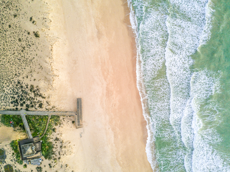Wooden pier leading to sandy beach and waves on Atlantic Ocean in Quinta do Lago, Almancil, Algarve, Portugalの写真素材