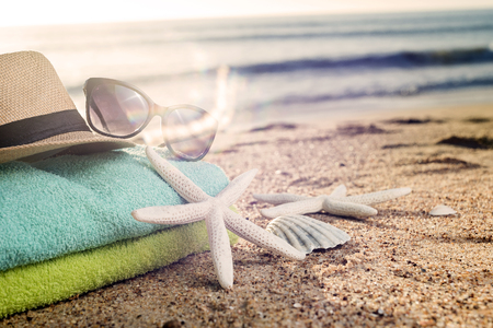 Summer accessories as colorful towels, straw hat, sun glasses and shells on the sandy beachの写真素材