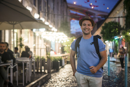 Happy young man in blue shirt walking on lively streets with restaurants at the evevningの写真素材