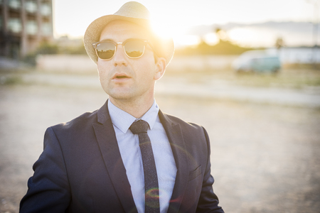 Lifestyle portrait of vintage looking young man in suit with sunglasses at sunsetの写真素材