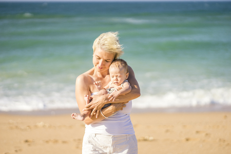 Attractive blond mother playing with 4 months old baby boy on the beachの写真素材