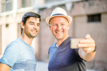 Two male friends taking selfie in the city using smartphoneの写真素材