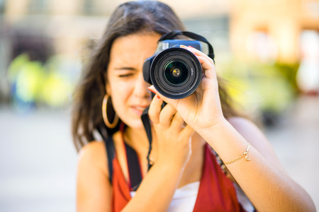 Beautiful teenager with long dark hair focuses on taking photography in urban scenicの写真素材
