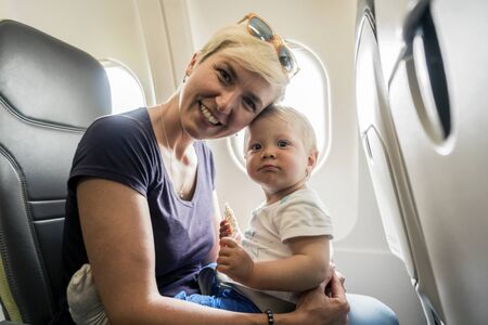Mother with small baby son playing in the airplane during the flightの写真素材