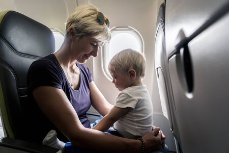 Mother with small baby son playing in the airplane during the flightの写真素材