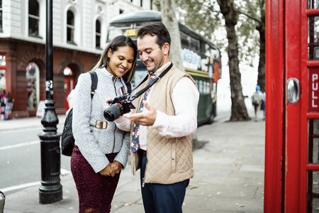 Happy travelling couple reviewing photos on theirs camera in London, UK. Double decker bus and red telephone booth in a frameの写真素材