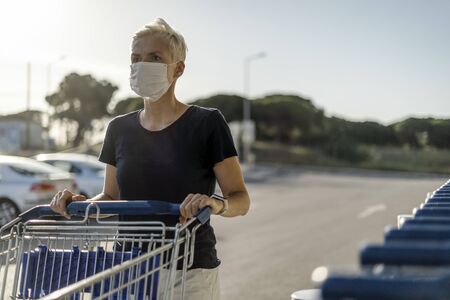 Woman wearing protective face mask with shopping cart in front of supermarketの写真素材