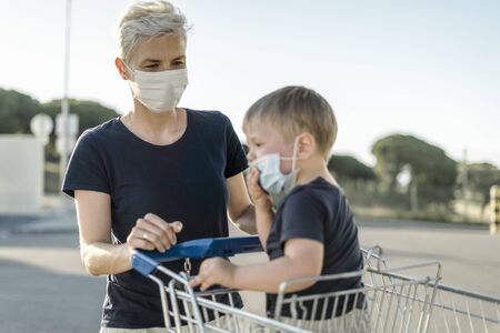 Mother with little son in shopping cart  wearing protective face masks going to do shopping in supermarketの写真素材