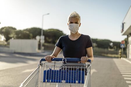 Woman wearing protective face mask with shopping cart in front of supermarketの写真素材