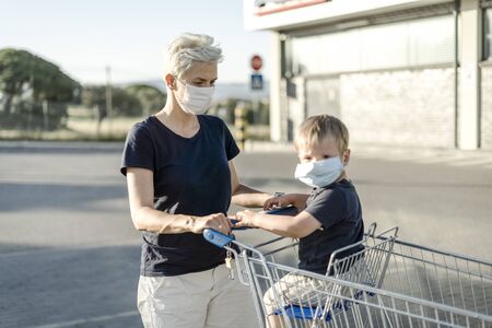 Mother with little son in shopping cart  wearing protective face masks going to do shopping in supermarketの写真素材