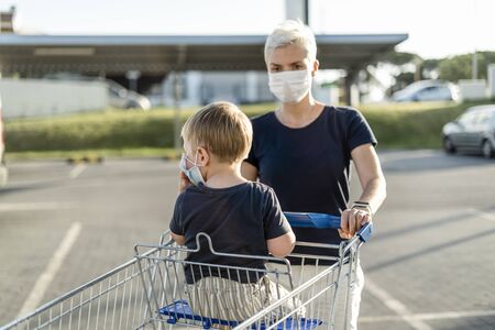 Mother with little son in shopping cart  wearing protective face masks going to do shopping in supermarketの写真素材