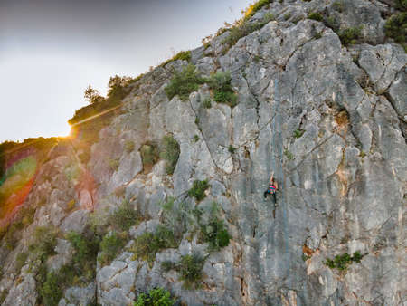 A woman in harness climbing a steep rock in Portugal