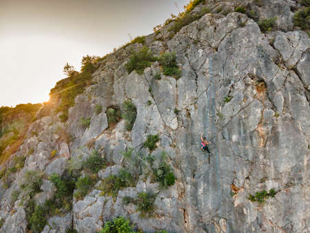 A woman in harness climbing a steep rock in Portugalの写真素材