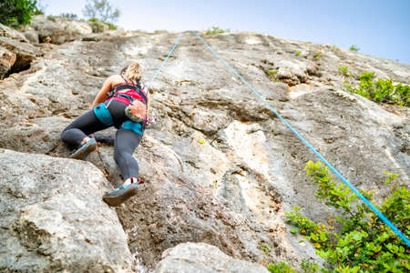A woman climbing a steep rock using climbing harnessの写真素材