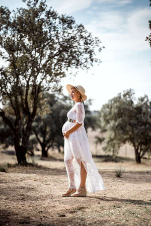 Pregnant woman wearing hat and white dress among cork treesの写真素材