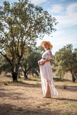 Pregnant woman wearing hat and white dress among cork treesの写真素材