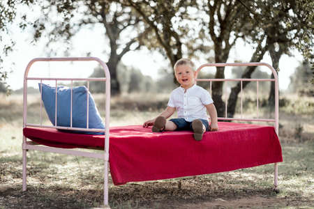 Cute small boy sitting on outdoor bed among cork treesの写真素材