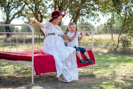 Expecting woman playing with her small son on outdoor bedの写真素材