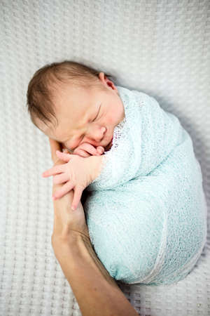 Cute sleeping newborn baby boy wrapped in blue laying on mother's handの写真素材