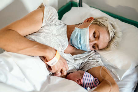 A new mother nursing her newborn little boy in facial mask during pandemic