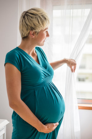 Pregnant woman with big belly looking through the windowの写真素材
