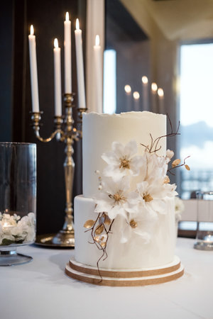 White wedding cake decorated with flowers and candles in the backgroundの写真素材
