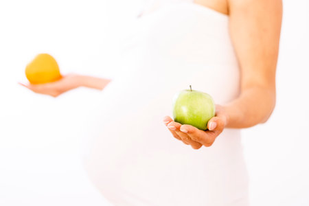 Pregnant woman holding an apple and an orange in her handsの写真素材