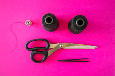 Black tailoring accessories as scissors, thread, tweezers and bobbin on pink backgroundの写真素材