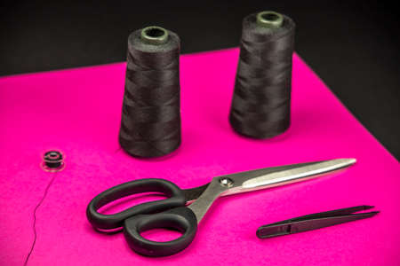 Black tailoring accessories as scissors, thread, tweezers and bobbin on pink backgroundの写真素材