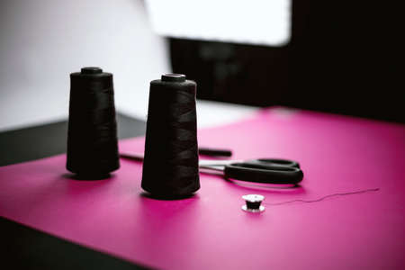 Black tailoring accessories as scissors, thread, tweezers and bobbin on pink backgroundの写真素材