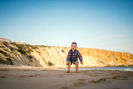 Small boy throwing stones on the beach by the sunset, Portugalの写真素材