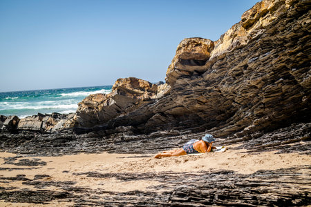 Elderly woman relaxing by rocks in Zambujeira Do Mar, Vicentina Coast Natural Park, Alentejo, Portugalの写真素材