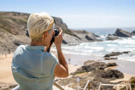 Woman taking a photo of a beautiful rocky beach in Zambujeira do Mar, Portugalの写真素材